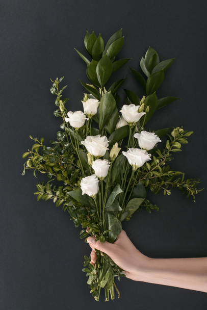 cropped image of female hand holding bouquet with eustoma and branches over black background  - Photo, Image