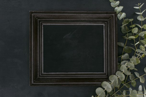 top view of vintage wooden frame with eucalyptus branches over black background - Photo, Image