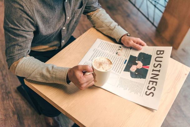 partial view of businessman with cup of coffee and business newspaper in cafe - Photo, Image