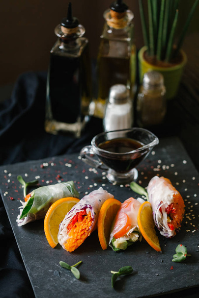 Rollos de primavera sobre plato negro complementados con semillas de girasol germinadas y salsa de soja
 - Foto, Imagen