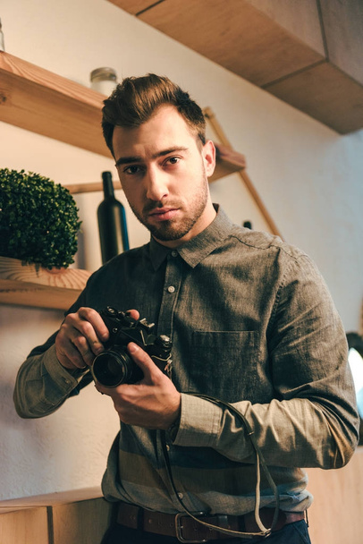 portrait of thoughtful man with photo camera standing in cafe - Foto, imagen