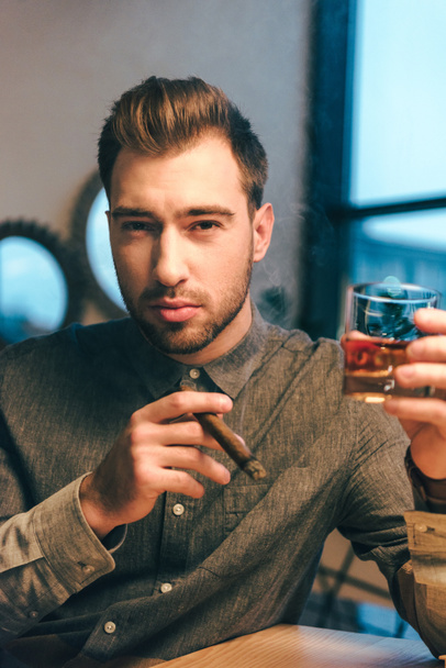 portrait of young man with glass of cognac and cigar in hands in cafe - Фото, зображення