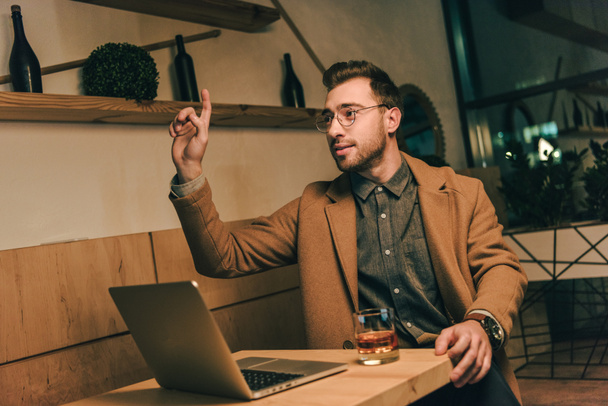 Portret van jonge man aan tafel met laptop aangedrongen ober in café - Foto, afbeelding