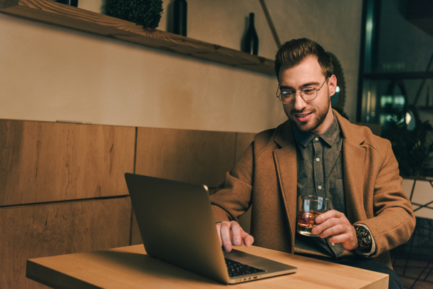 mosolygó ember, pohár whisky használ laptop, kávézó asztal portréja - Fotó, kép