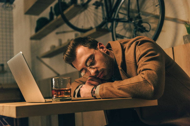 zmęczony człowiek spanie na stole z szklanką whisky i laptopa w kawiarni - Zdjęcie, obraz