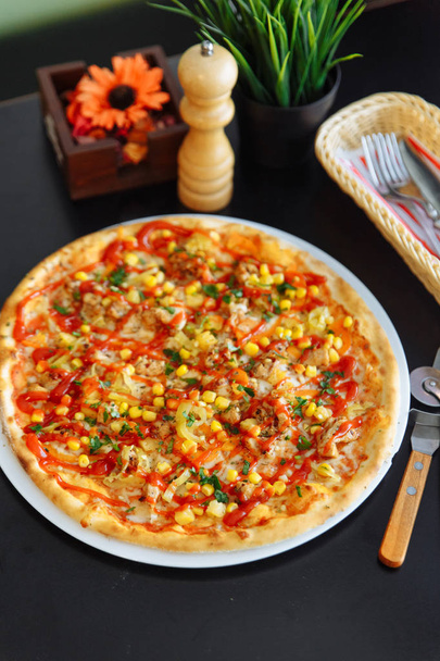 Pizza italiana gourmet en plato blanco con cuttery, cortador de pizza, molinillo de pimienta, flor y hierba en jarrones
 - Foto, Imagen