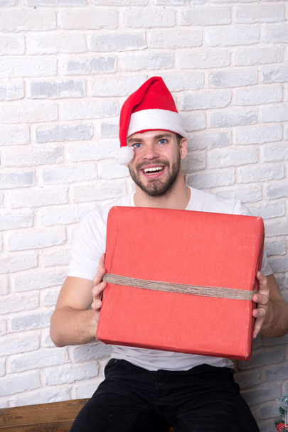 Macho in christmas hat smile with wrapped present - Zdjęcie, obraz