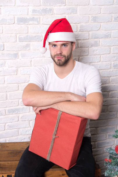Macho in christmas hat hold wrapped present - 写真・画像