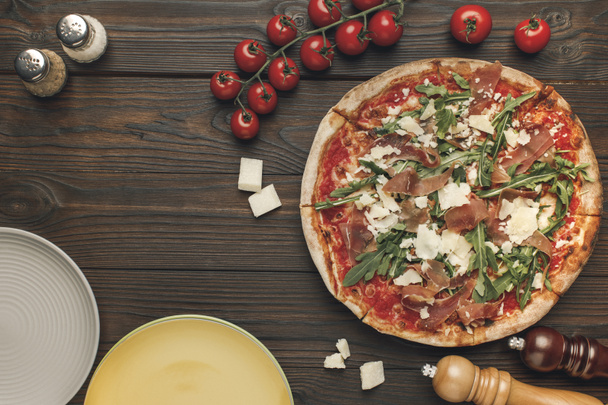vista superior de pizza italiana, tometões de cereja e pratos vazios em talbetop de madeira
 - Foto, Imagem
