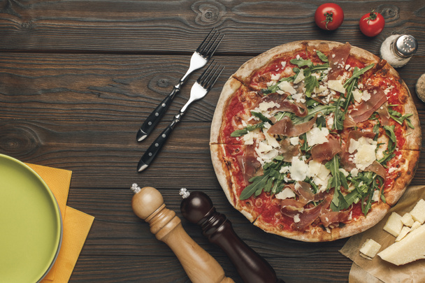 flat lay with arranged italian pizza, cutlery and various ingredients on wooden surface - Foto, Bild
