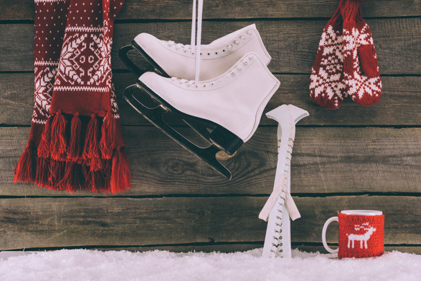 red scarf with gloves and white skates hanging on striped wall  - Photo, Image