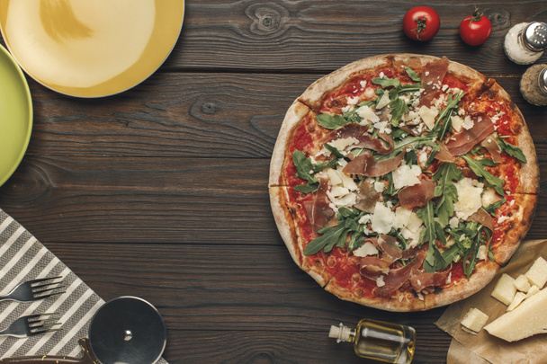 flat lay with arranged italian pizza, cutlery and various ingredients on wooden surface - Photo, Image