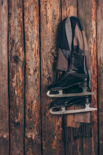 木製の壁にぶら下がっている黒いスケートのペアと暖かいスカーフ - 写真・画像