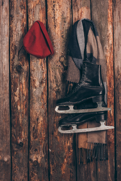 red hat with scarf and black skates hanging on wooden wall - 写真・画像