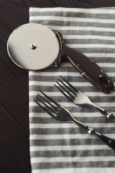 Close-up van stalen vorken en pizza cutter op linnen servet - Foto, afbeelding