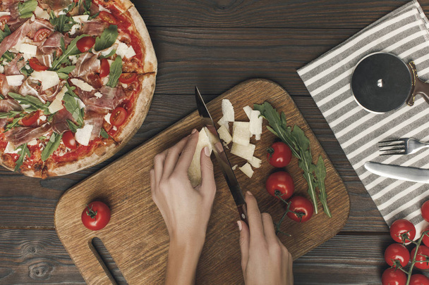 częściowy widok kobiety cięcia sera podczas gotowania domowe włoska pizza - Zdjęcie, obraz