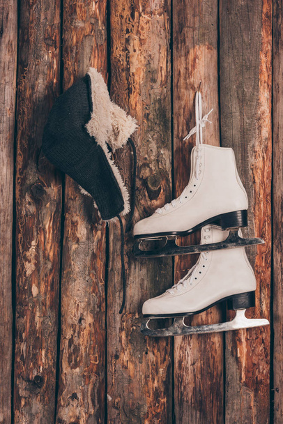 hat with ear flaps and pair of skates hanging on wooden wall - Photo, Image