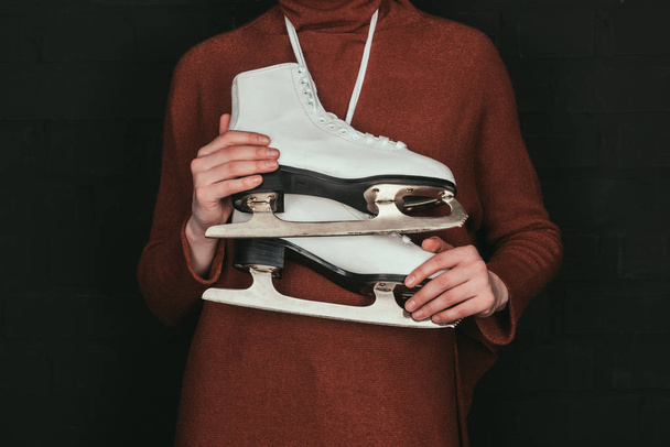 cropped image of woman in brown sweater holding skates isolated on black - Foto, afbeelding