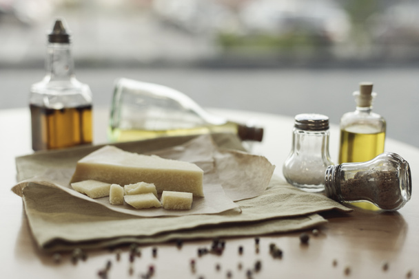 selective focus of piece of cheese on napkin and oil in bottles  - Foto, afbeelding