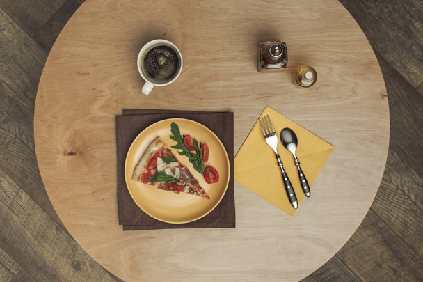 posa piatta con pezzo di pizza disposto su piatto, tazza di tè e posate su tavolo in legno
 - Foto, immagini