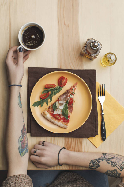 részleges kilátás nyílik nő ül asztal pizza darab lemez és csésze kávé - Fotó, kép