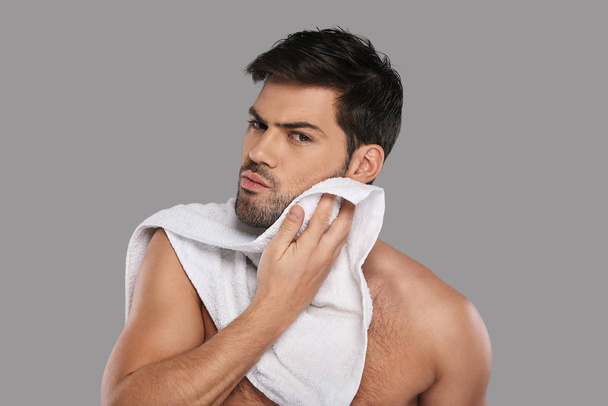 Handsome young man wiping face with towel against grey background - Foto, Imagen