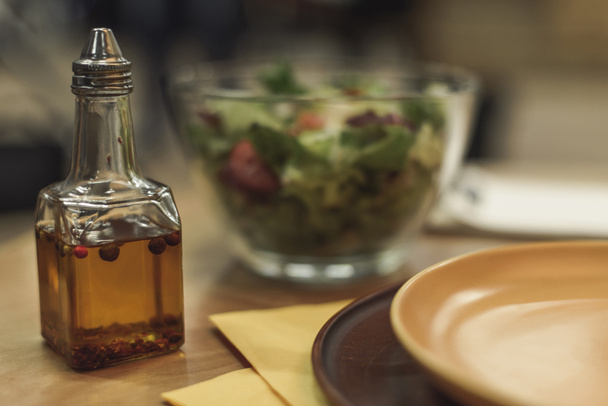 selective focus of oil in bottle, plates and salad in bowl on table - Photo, image