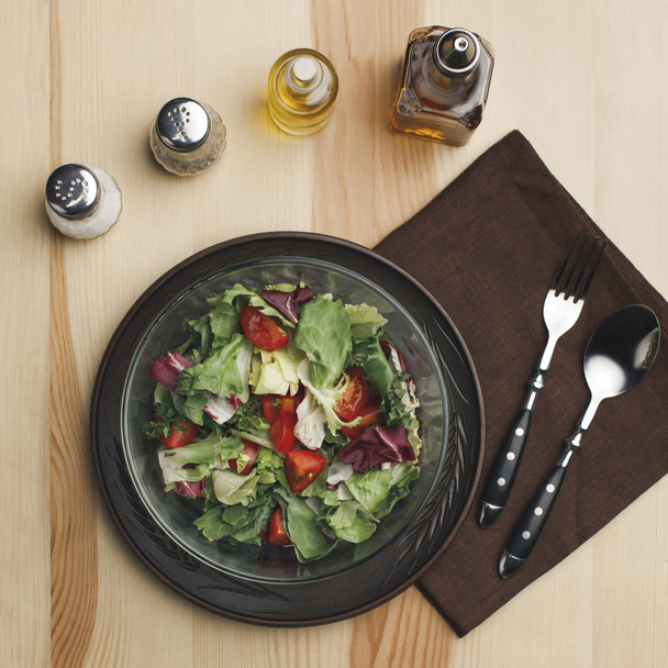 vlakke leggen met gearrangeerde salade in de kom, specerijen en flessen van olieverf op houten oppervlak - Foto, afbeelding