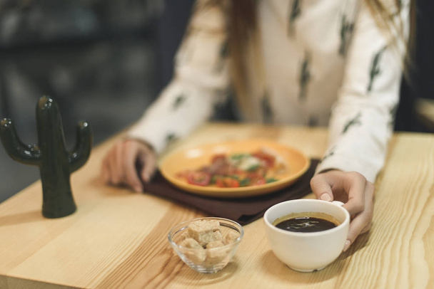 вибірковий фокус жінки, що сидить за столом з чашкою кави та шматочком піци на тарілці
 - Фото, зображення