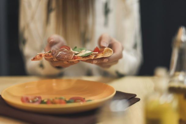 częściowy widok kobieta trzyma kawałek pizzy włoskiej w ręce - Zdjęcie, obraz