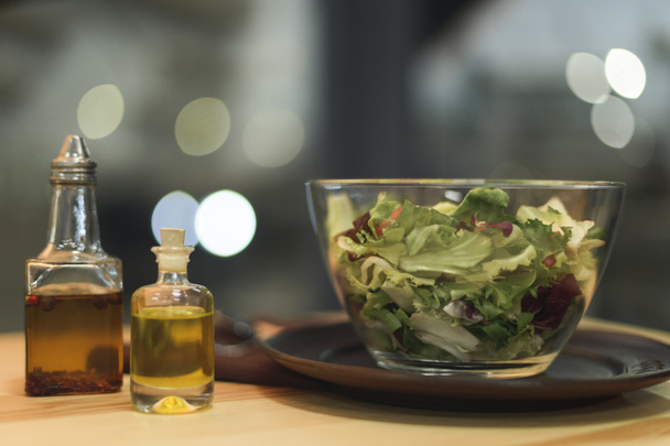 close up view of fresh salad in bowl and oil in bottles on wooden surface - Foto, Imagem