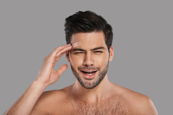 shirtless unhappy brunette man touching adhesive bandage on his forehead - Foto, Imagen