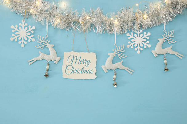 Рождественский фон с гирляндой, белыми оленями и белыми снежинками на светло-голубом фоне
. - Фото, изображение