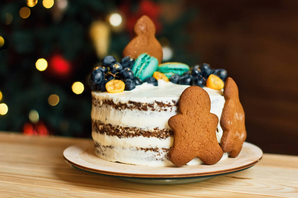 Beautiful decorated cake with gingerbread men for Christmas table on New Year bokeh background. Preparing for a family celebration - Foto, Imagem