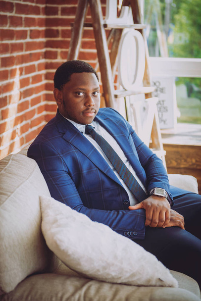 African american man in blue suit sitting on sofa - 写真・画像