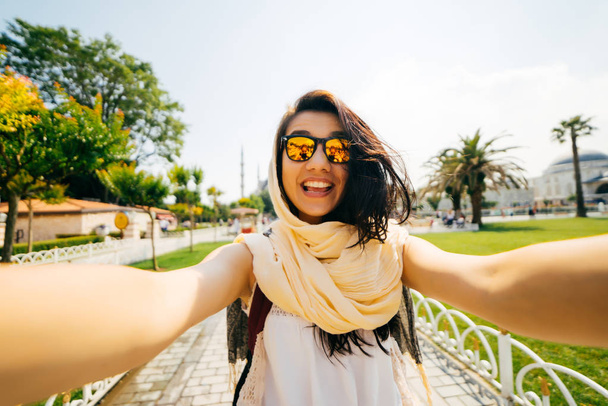 A bright happy girl in a scarf makes a selfie, a photo of herself. Exchange student on vacation - Фото, изображение