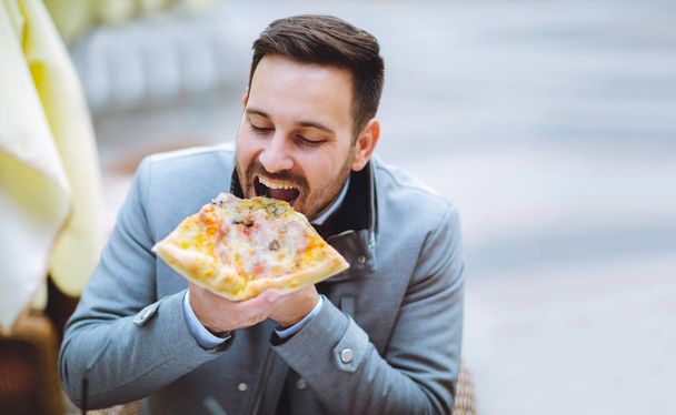 handsome young man eating slice of pizza in cafe - Photo, Image