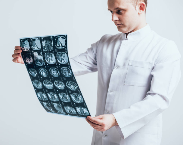 Male octor attentively examines the MRI scan before white wall - Photo, image