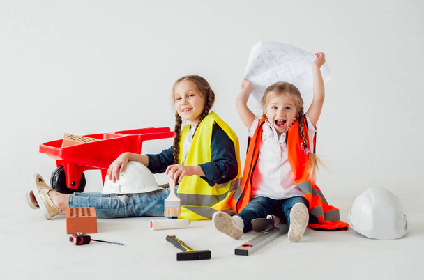 Две маленькие веселые девочки с косичками играют в ремонте или строительстве на белом
 - Фото, изображение