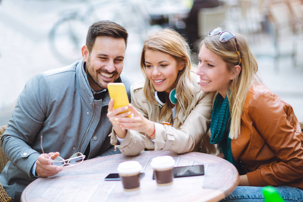 Gruppe von drei glücklichen Freunden mit Smartphone im Café - Foto, Bild