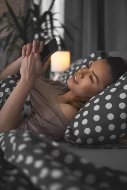 Młoda piękna kobieta przy użyciu telefonu, relaksując się w łóżku  - Zdjęcie, obraz