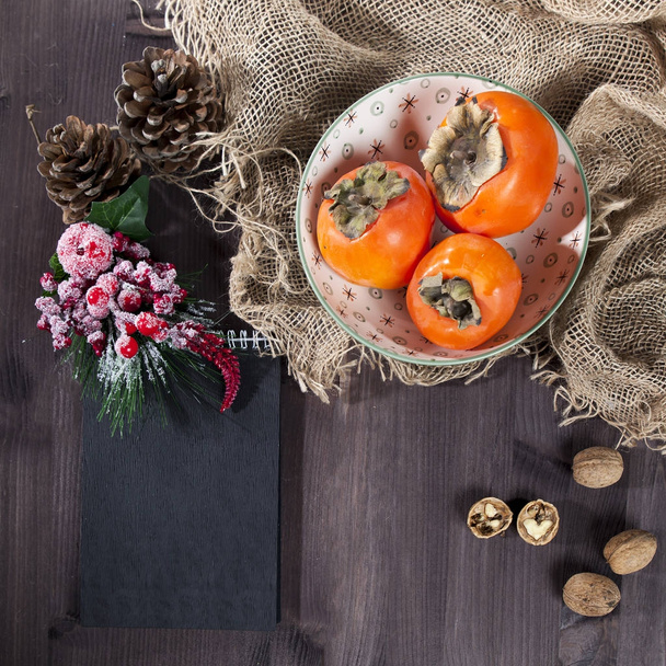 the persimmon in a plate on a napkin made of canvas on a dark wooden table - Φωτογραφία, εικόνα