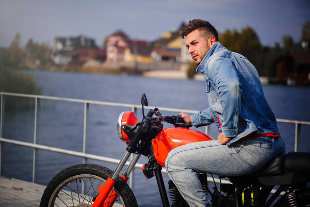 μεγάλη πορτρέτο ενός νεαρού άνδρα σπορ της μόδας σε μια μοτοσικλέτα, ένα ζεστό πυροβόλησε, τέλη του φθινοπώρου - Φωτογραφία, εικόνα