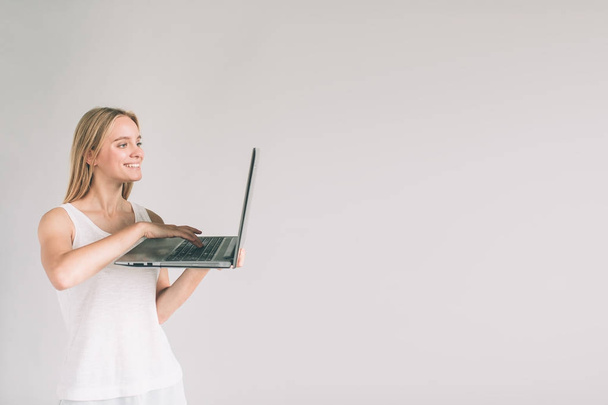 Woman holding laptop computer isolated on gray. Girl in white shirt, studio shot - Fotoğraf, Görsel