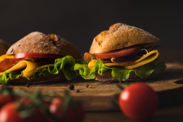 sandwiches with cheese on wooden board on table with cherry tomatoes on foreground - Photo, image