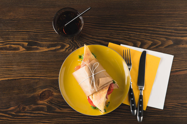 top view of panini on yellow plate with fork and knife on napkins - Zdjęcie, obraz