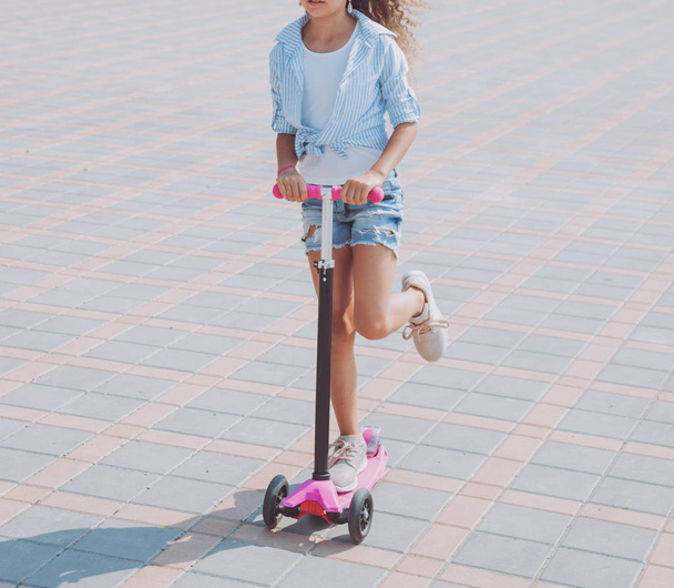 Маленькая девочка катается на скутере по улице в солнечный день
 - Фото, изображение