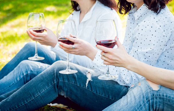 Three young girls enjoing red wine in park. - Zdjęcie, obraz