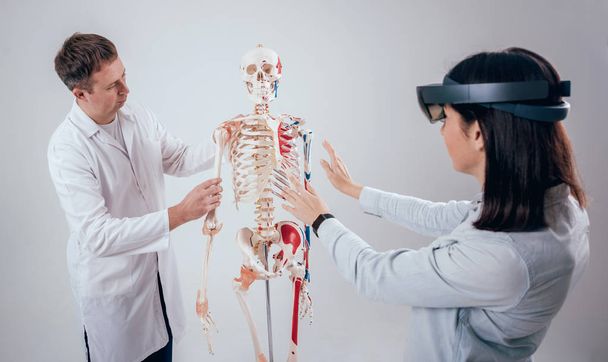 Doctor uses augmented reality goggles and human skeleton for teaching student - Foto, afbeelding