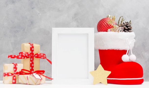 Bright christmas mock up with photo frame: festive gift boxes, toys, and fir-cones in red santa's boot New year concept. Text space. Greeting card template - Fotografie, Obrázek